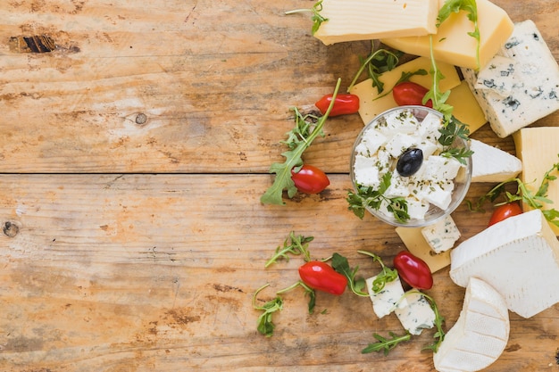 Foglie di rucola con pomodori; blocchi di formaggio sul contesto strutturato in legno