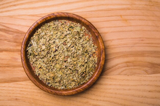 Foglie di tè asciutte verdi aromatiche sul piatto contro fondo di legno
