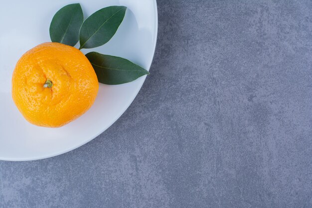Foglie e arance succose sul piatto sul tavolo di marmo.