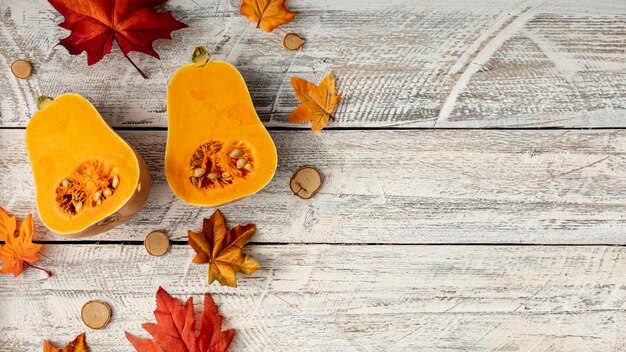 Foglie e zucca divisa in due su fondo di legno bianco