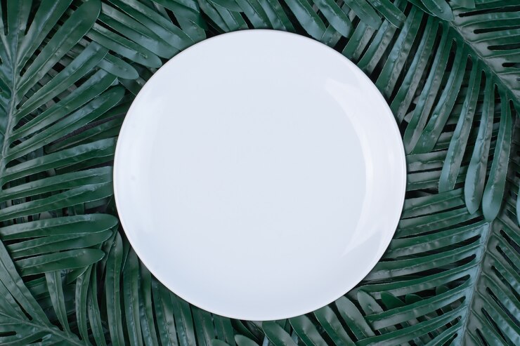 Foto gratuito foglie verdi artificiali intorno al piatto bianco.