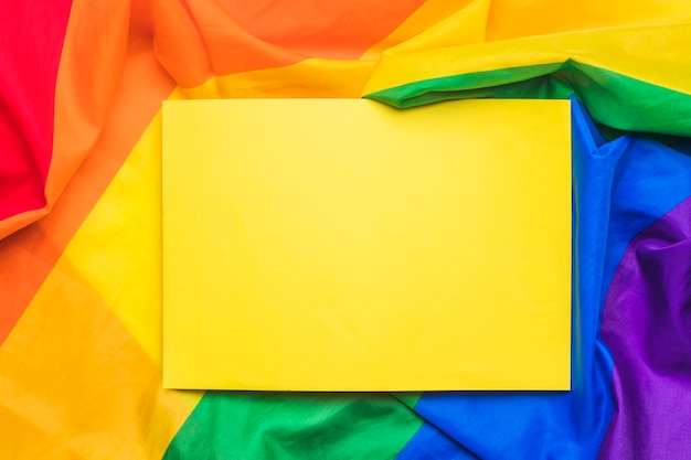 Foglio di carta vuoto giallo sulla bandiera LGBT stropicciata