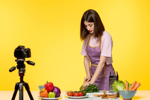 Food blogger giovane ragazza in grembiule rosa che registra video per i social media che tagliano la lattuga