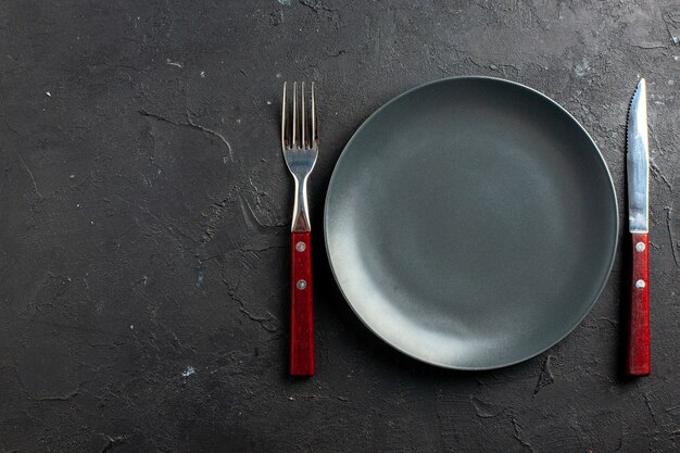 Forchetta e coltello del piatto nero di vista superiore sulla superficie nera con lo spazio della copia