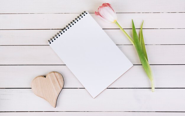 Forma di cuore in legno; blocchetto per appunti e tulipano a spirale in bianco sulla tabella di legno