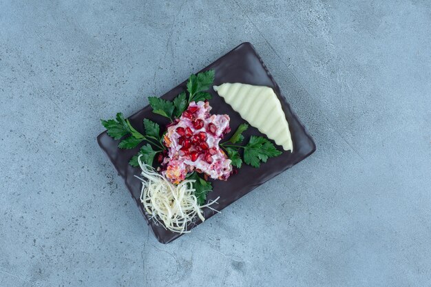 Formaggio a fette e grattugiato su un piatto nero con una piccola porzione di insalata, su marmo.