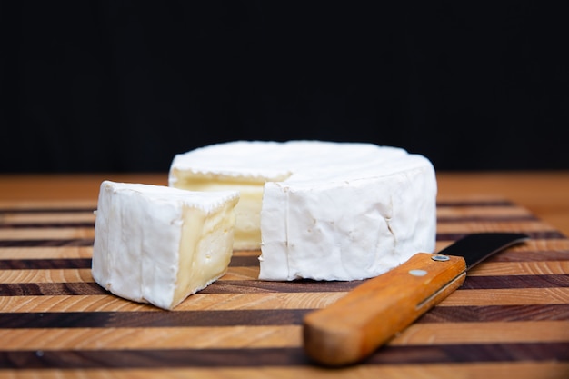 Formaggio a pasta molle e coltello che mettono su tavola di legno