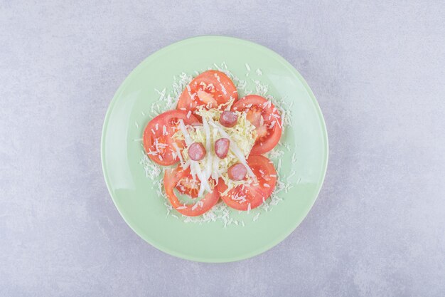 Formaggio grattugiato con salsicce e pomodoro sul piatto verde.