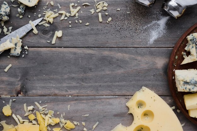 Formaggio grattugiato e fette sullo scrittorio di legno grigio per la scrittura del testo