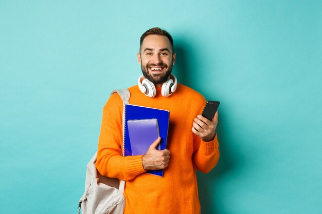 Formazione scolastica. Bello studente maschio con le cuffie e lo zaino, utilizza lo smartphone