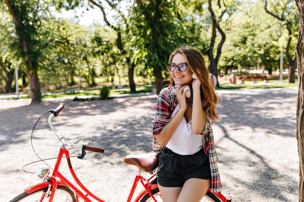 Formosa ragazza carina in posa con la bicicletta nel parco. Felice signora europea trascorrere la mattina d'estate all'aperto.