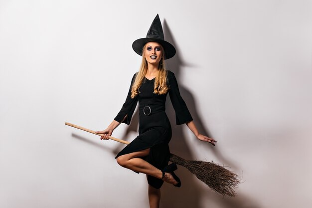 Formosa strega piacevole seduta sulla sua scopa. adorabile mago femmina in cappello magico.