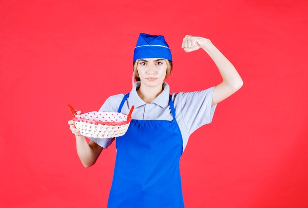 Fornaio femminile in grembiule blu che tiene un cestino del pane con un asciugamano rosso all'interno e che mostra il segno della mano di piacere