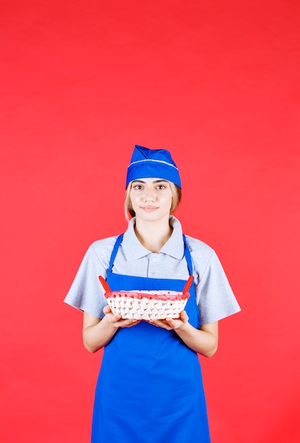 Fornaio femminile in grembiule blu che tiene un cestino del pane con un asciugamano rosso all'interno