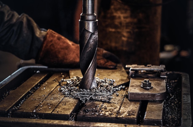 Foro di perforazione nel metallo con trapano gigante in fabbrica di acciaio da parte di un lavoratore maschio.