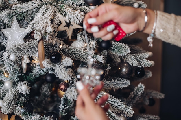 Foro ritagliato delle mani della signora che tengono un bellissimo giocattolo di cervo vicino all'albero di Natale. Concetto di capodanno