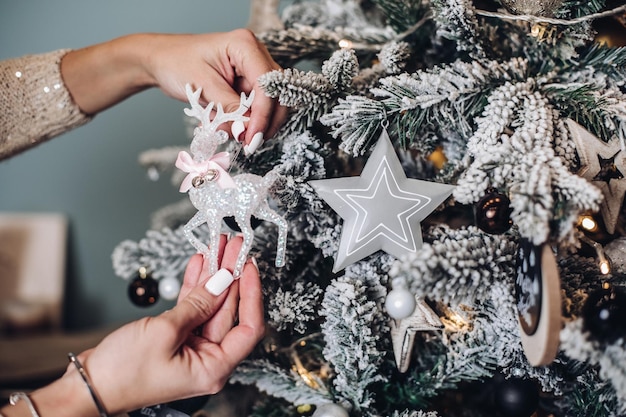 Foro ritagliato delle mani della signora che tengono un bellissimo giocattolo di cervo vicino all'albero di Natale. Concetto di capodanno