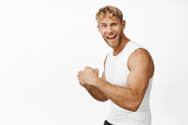 Forte atleta maschio flex bicipite che mostra forti maschi sulle braccia gridando gioioso allenamento in palestra in piedi su sfondo bianco