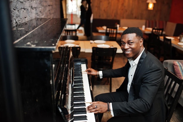 Forte potente uomo afroamericano in abito nero suonare il pianoforte