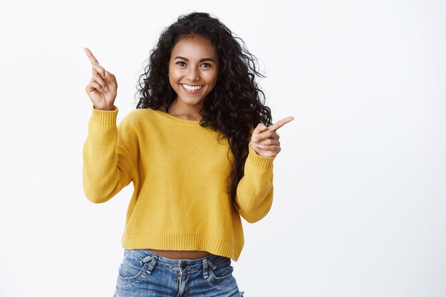 Fortunata ragazza afroamericana allegra con un sorriso divertito e compiaciuto che punta di lato, mostrando lo spazio della copia sinistra e destra con stupore e gioia, promuove volentieri un'offerta interessante, indicando i banner del prodotto