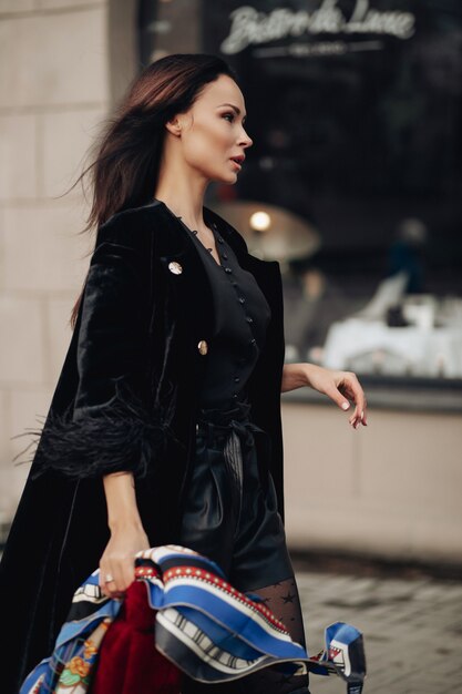 Foto a figura intera di bella donna elegante che cammina per strada mentre indossa una sciarpa di seta sulla testa. Concetto di bellezza e moda