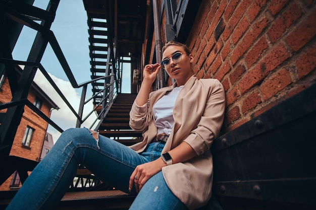 Foto ad angolo basso di una donna sfacciata casual in occhiali da sole e denim nel cortile sul retro.