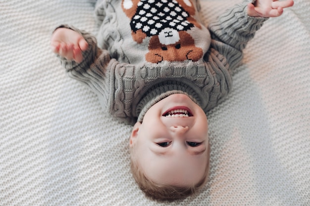 Foto capovolta di un adorabile bambino in maglione caldo sdraiato sul letto e ridendo