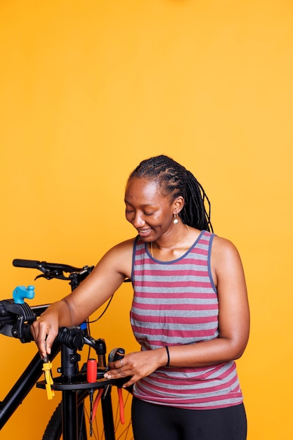 Foto che mostra una donna di colore sana e atletica che tiene in mano strumenti professionali e si prepara per la manutenzione annuale della bicicletta. Giovane donna che posiziona attrezzature specializzate sul cavalletto per la riparazione di biciclette.