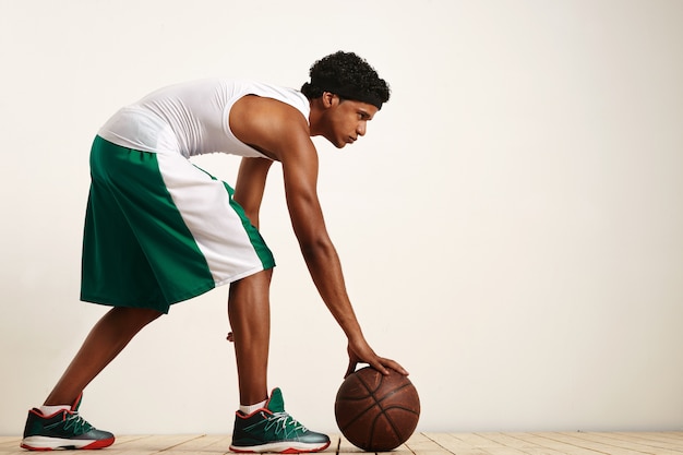 Foto del colpo posteriore del giocatore di basket che tiene la palla al suo fianco su bianco