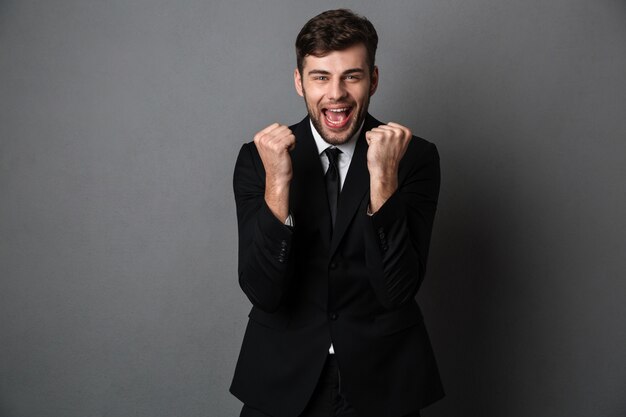 Foto del primo piano dell'uomo attraente felice in vestito classico che mostra gesto del vincitore,