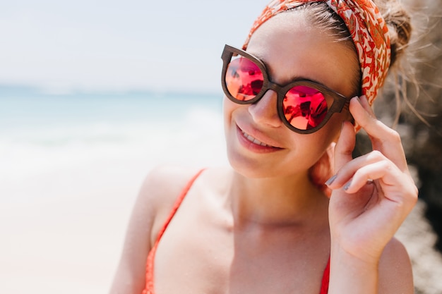 Foto del primo piano della meravigliosa donna abbronzata in grandi bicchieri scintillanti. Colpo esterno di sorridente ragazza caucasica divertendosi in una giornata di sole in mare.