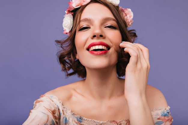 Foto del primo piano della risata entusiasta della giovane donna. modella femminile di buon umore in cerchietto di fiori.