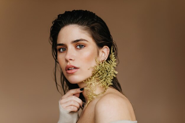 Foto dell'interno della signora europea ispirata con la pianta. Interessato ragazza dai capelli neri in posa sulla parete marrone con fiore.