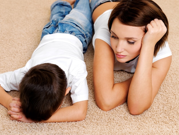 Foto della giovane madre e del figlio disobbediente e colpevole che piange sdraiato sul pavimento