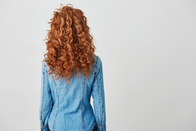 Foto della ragazza con capelli ricci rossi che stanno di nuovo alla macchina fotografica. Copia spazio.