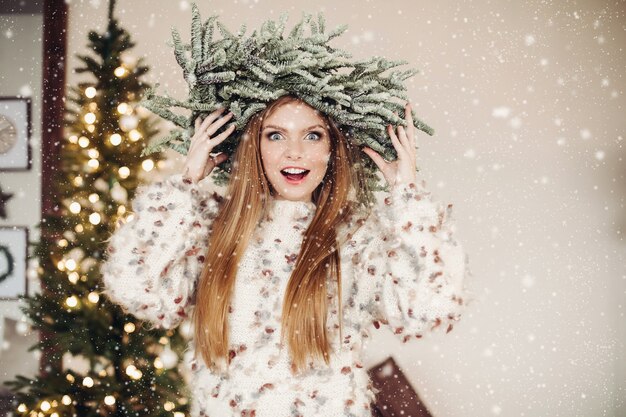 Foto della vita di una signora dai capelli rossi eccitata che indossa una corona di rami di abete in uno sciame di fiocchi di neve