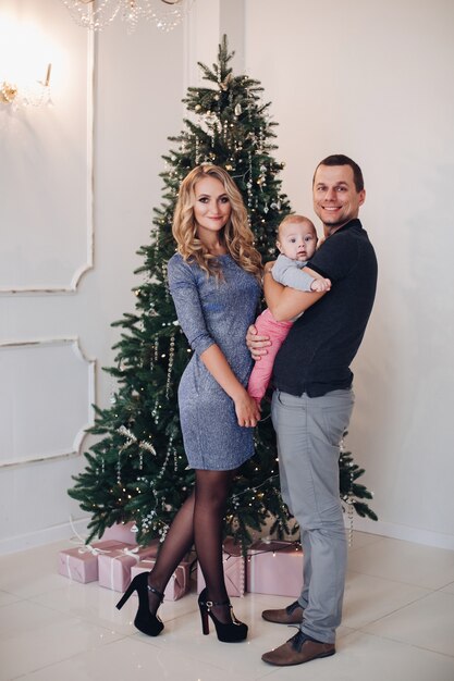 Foto di concetto di nuovo anno di una giovane famiglia felice di due genitori e un bambino in posa vicino all'albero di Natale