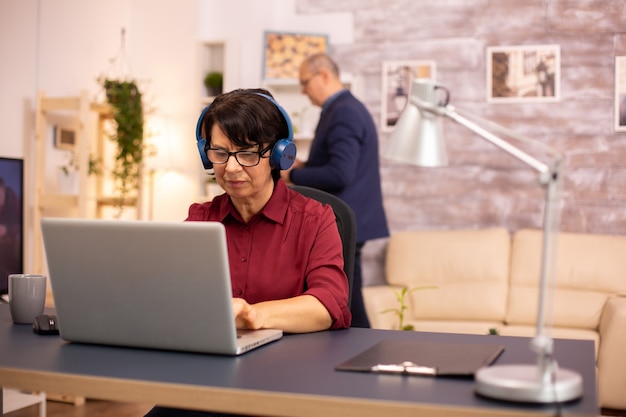 Foto di concetto di vecchia signora che utilizza la tecnologia moderna. Usa cuffie wireless e un laptop