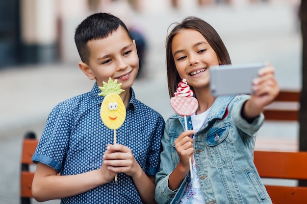 Foto di due bambini felici che fanno selfie un giorno d'estate con dolci sulle mani e sorridenti.