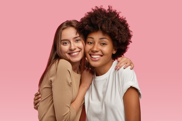 Foto di due giovani modelli di bell'aspetto che stanno vicini, si abbracciano e si divertono insieme, vestiti con abiti casual, modello su uno spazio rosa