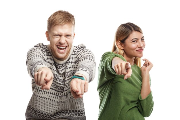 Foto di felicissimo estatico giovane coppia caucasica barbuto uomo e donna bionda in piedi uno accanto all'altro, avendo eccitato sguardi felici e puntando le dita, scegliendo te