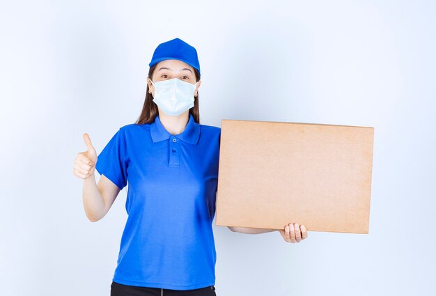 Foto di giovane donna in uniforme con scatola di carta che mostra pollice in su.