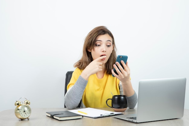 Foto di impiegato femminile seduto alla scrivania e utilizzando il telefono cellulare. Foto di alta qualità