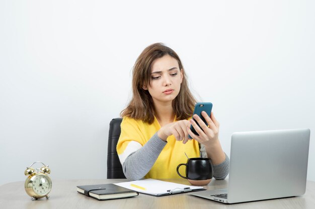 Foto di impiegato femminile seduto alla scrivania e utilizzando il telefono cellulare. Foto di alta qualità