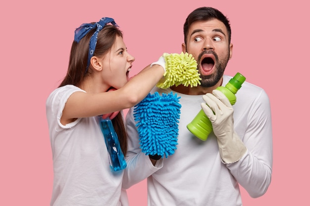 Foto di marito e moglie sposati puliscono insieme la casa, posano con detersivo, spugne, indossano abiti casual