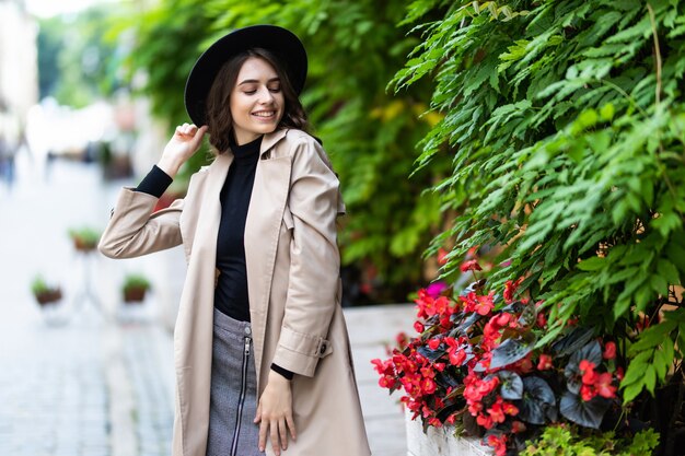 Foto di moda all'aperto di giovane donna graziosa in abito elegante e cappello nero che cammina per strada