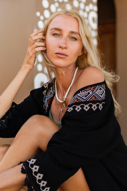 Foto di moda di bella donna bionda in abito estivo boho in posa all'aperto. Indossa una collana alla moda. Umore tropicale.