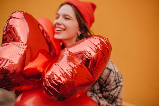 Foto di palloncini rossi e ragazza felice che li ha ricevuti in regalo su sfondo arancione