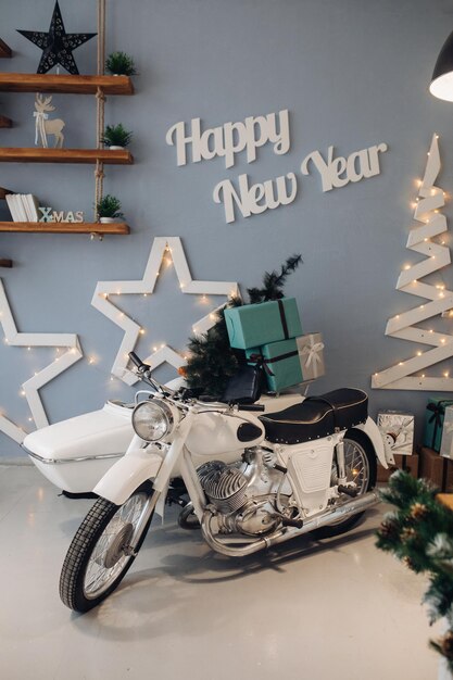 Foto di stock di motocicletta bianca con albero di Natale in miniatura e regali di Natale avvolti nella culla. Interni d'atmosfera per il giorno di Natale. Capodanno 2020.