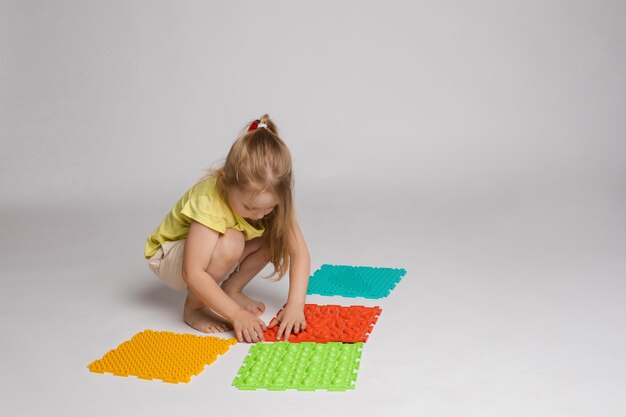 Foto di stock di un bambino che gioca con tamponi di gomma colorati e luminosi per migliorare e sviluppare le capacità motorie sul pavimento. È seduta sulle anche in studio